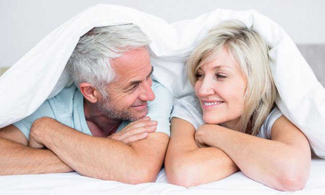 ベッドに横たわって笑顔で見合っている中年期の夫婦｜副腎疲労blog